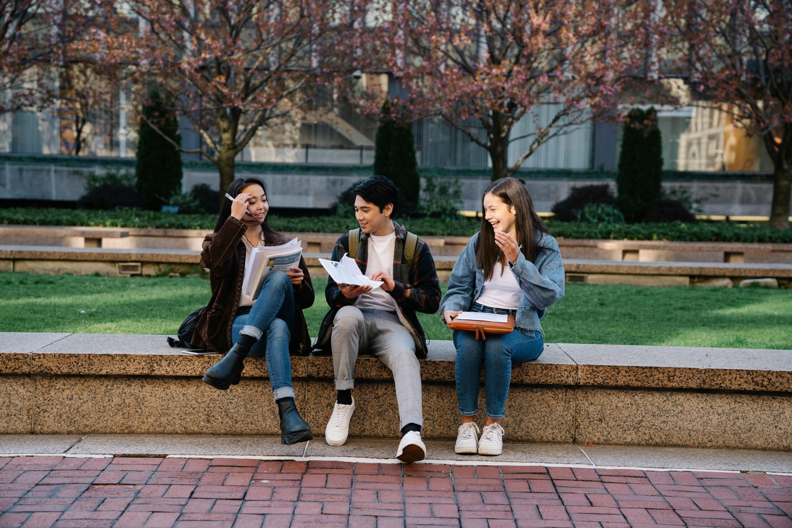 Three students sitting outdoors on a university campus with books